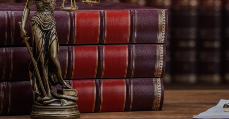 A laptop, books and a gavel on a wooden table.